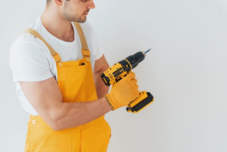 Handyman in yellow uniform standing against white wall with automatic screwdriver